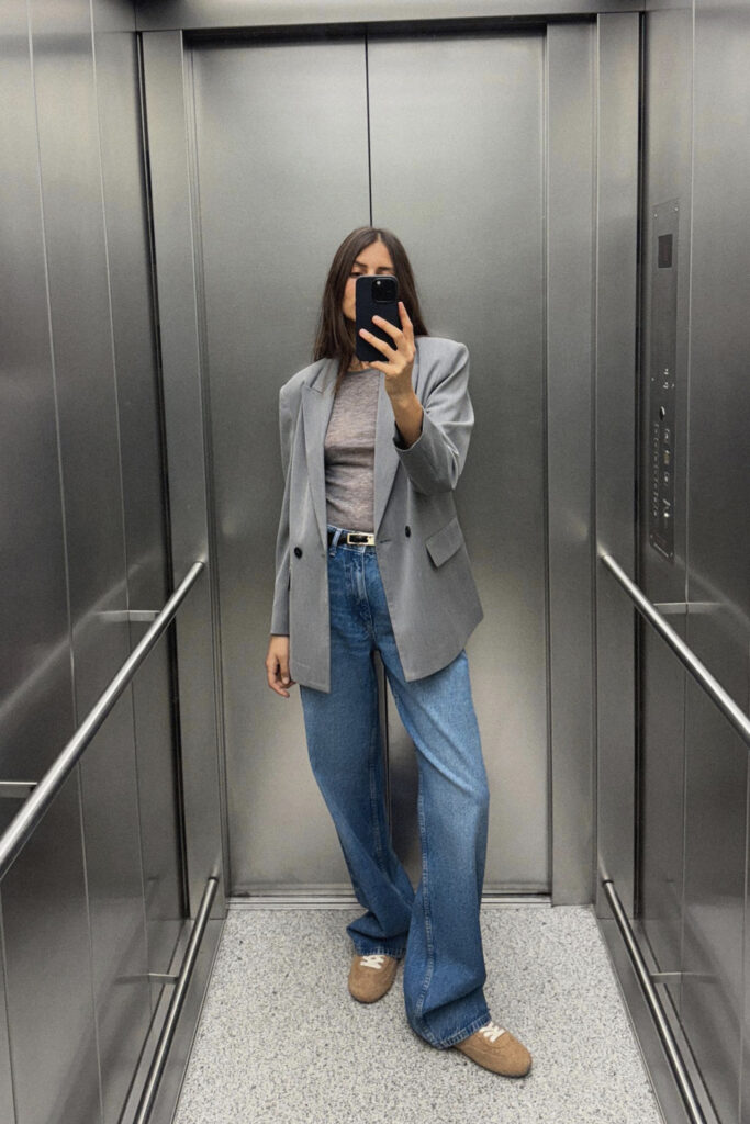 7 besten Fashion-Essentials: Frau im Lift macht ein Selfie und trägt Jeans und einen grauen Blazer