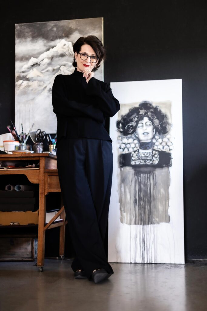 Ulrike Maria Kleber in ihrem Atelier, stehend vor einem ihrer Werke – eine Verbindung von Persönlichkeit und künstlerischer Handschrift.