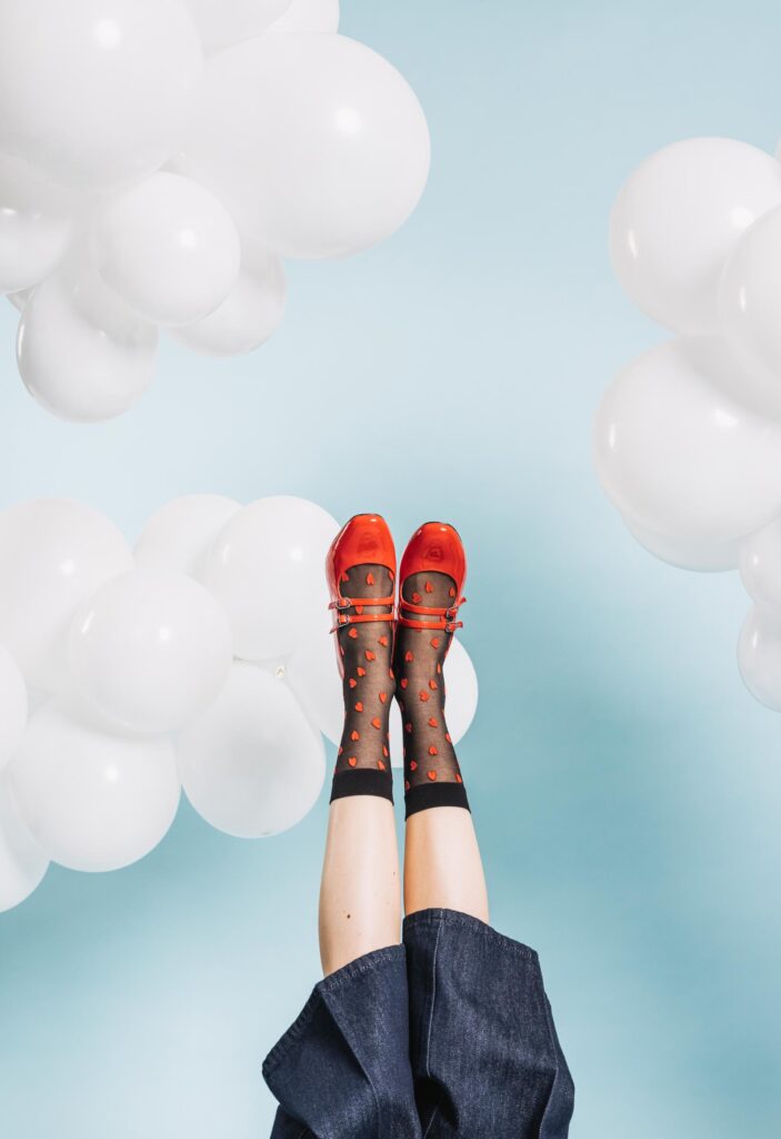 Spielerisches Fashion-Foto mit roten Sandalen vor einem hellblauen Hintergrund mit schwebenden Luftballons – Frühling für den Dornbirner Messepark.