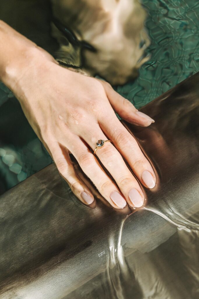 Nahaufnahme einer Hand mit Ring, die sanft die Wasseroberfläche streift – Sinnbild für Ästhetik und Wahrnehmung.