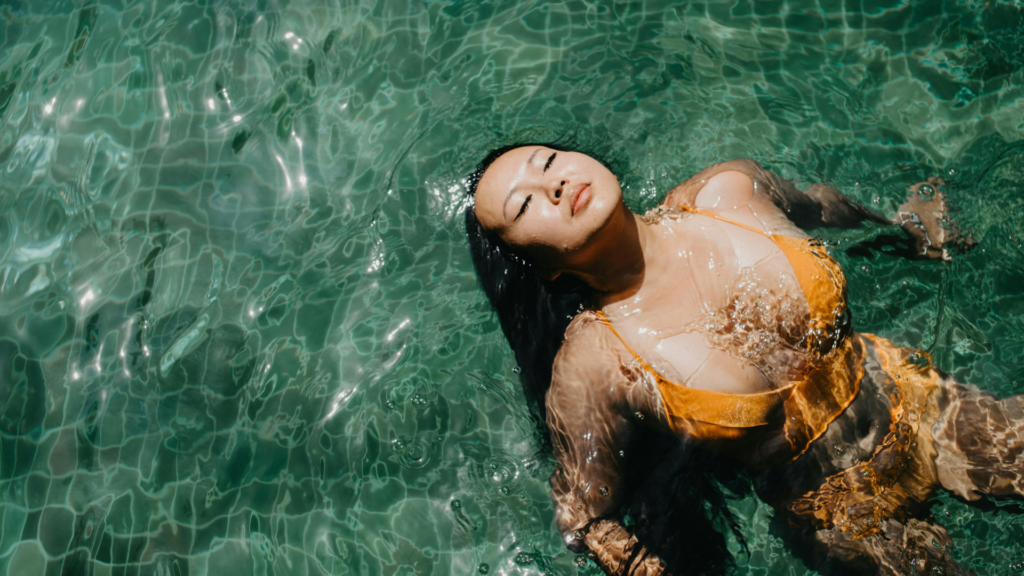 August Monatshoroskop 2025. Eine Frau im Bikini lässt isch im Pool treiben und sieht nach oben