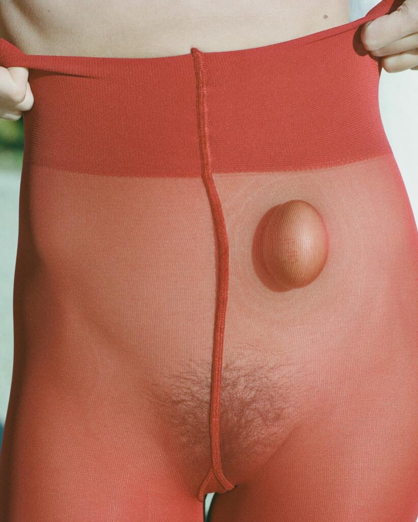 Provokantes Kunstfoto der Ritsch Sisters: Ein weiblicher Körper in roter Strumpfhose mit Ei – Symbol für Fragilität, Fruchtbarkeit und genderpolitische Aussagen.