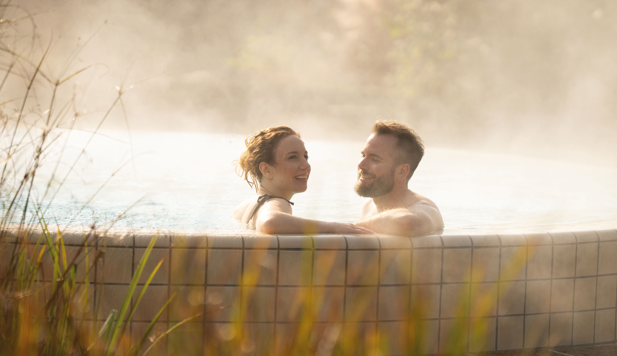 Ausflugsziele Steiermark: Ein junges Pärchen genießt Zweisamkeit in einem sonnigen Thermalbecken im Freien.