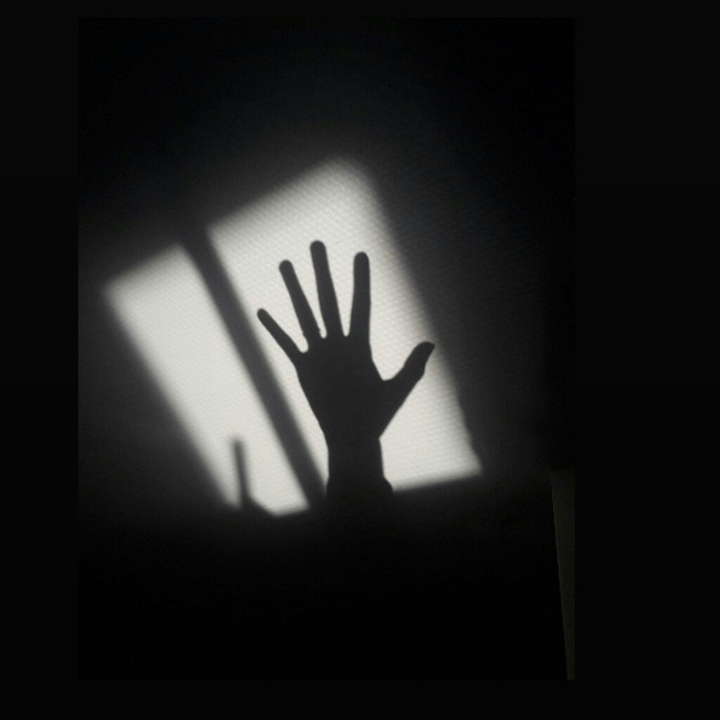 Schatten-Hand greift vor weißer Mauer in die Luft.