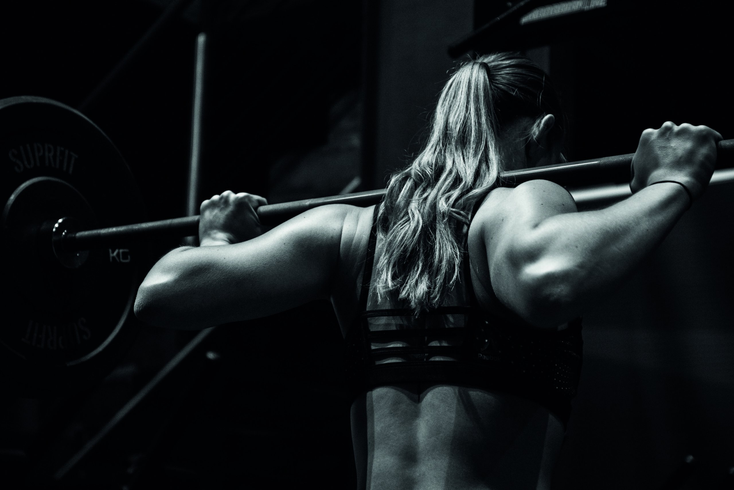 Frau von hinten mit einer Langhantel auf den Schultern