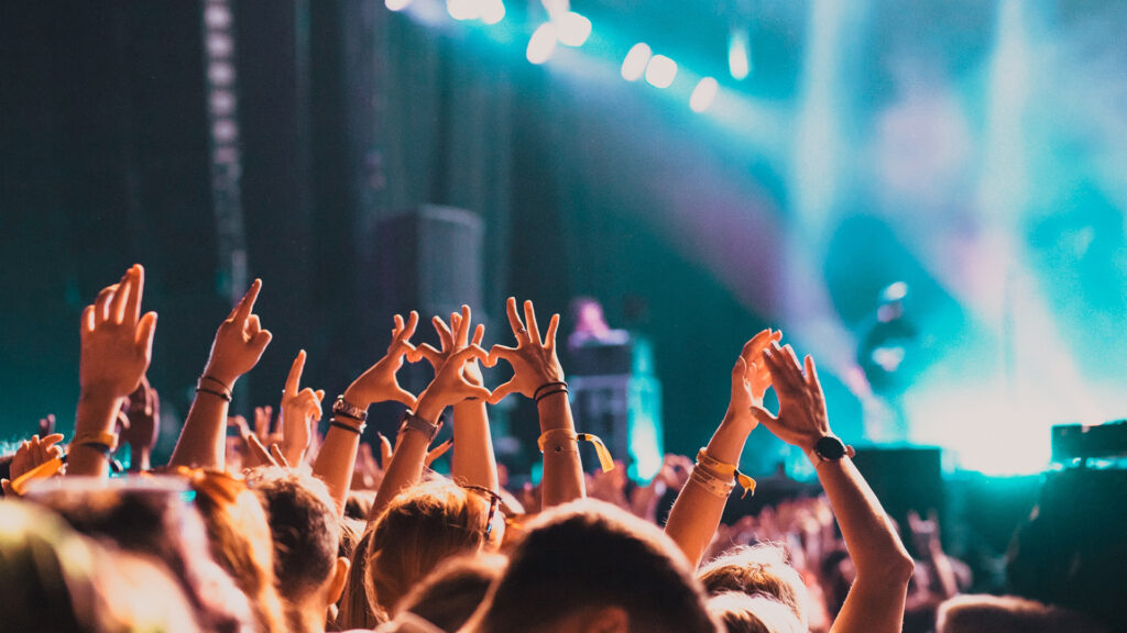 Events Österreich: Publikum bei Konzert mit erhobenen Händen vor beleuchteter Bühne – Live-Musik-Event.
